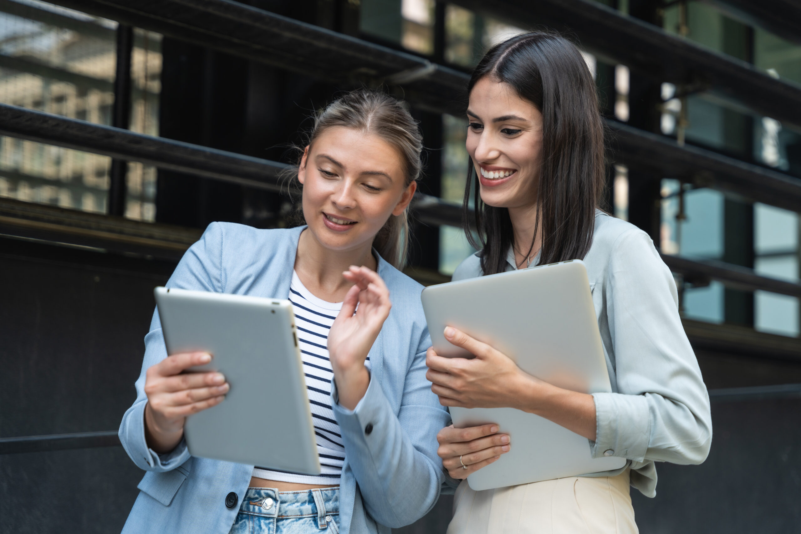 Two business women out of office building with laptop and digita
