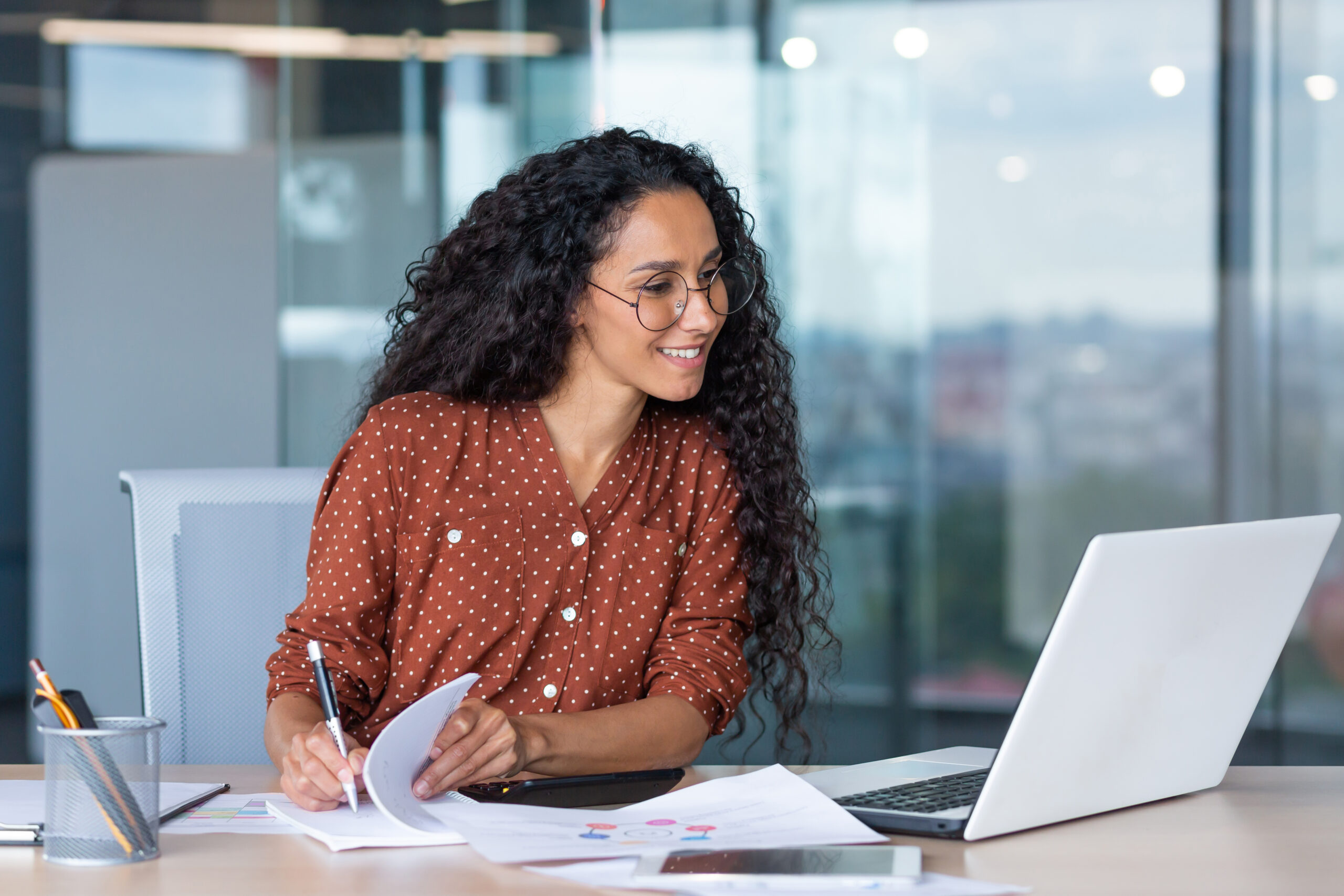 Young latin american businesswoman working inside office with documents and laptop, worker paperwork calculates financial indicators smiling and happy with success and results of achievement and work